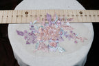 a close-up view of a delicate floral embroidery on a white fabric, with a ruler placed over it to provide a size reference.