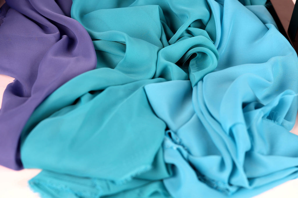 a close-up view of a pile of fabric, with a mix of blue and purple colors. The fabric appears to be crumpled and wrinkled, suggesting it may be used for clothing or textile purposes.