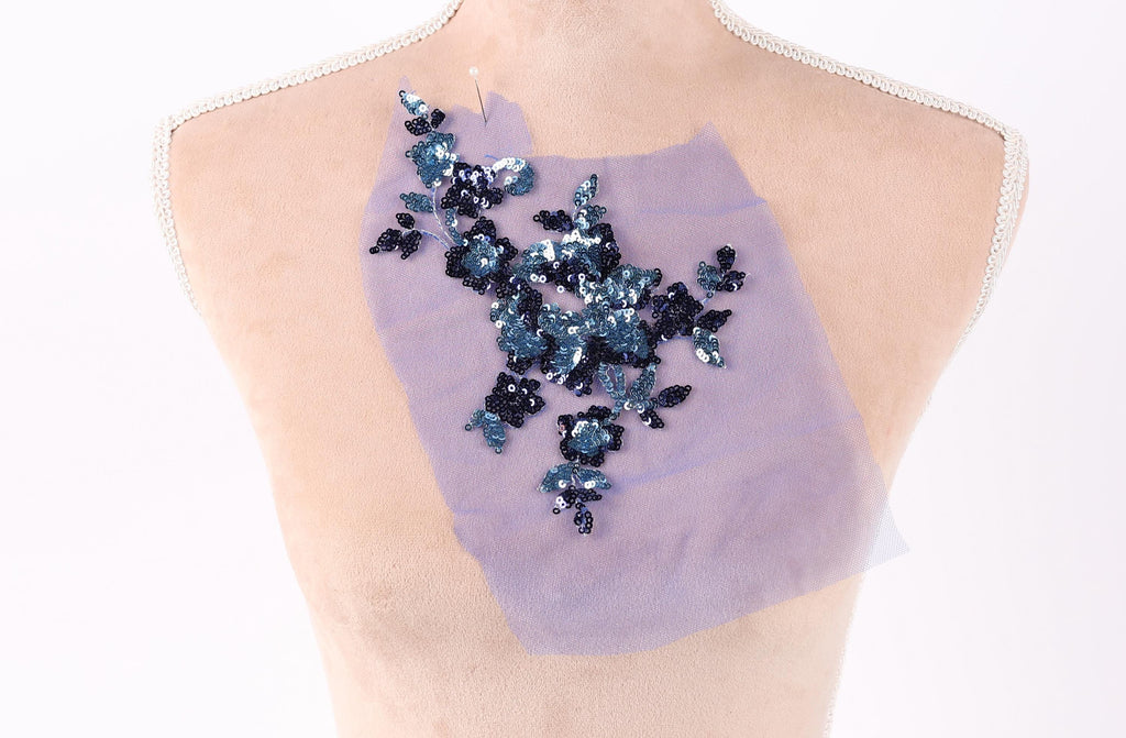 a mannequin torso with a purple fabric draped over it, featuring a floral pattern made of sequins in shades of blue and black.