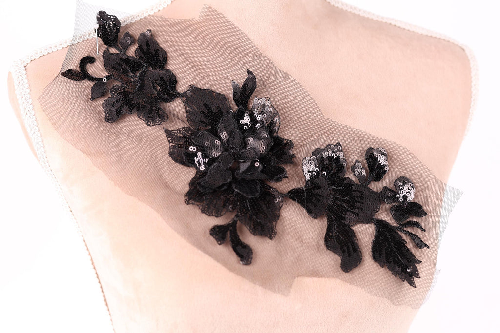 a close-up view of a delicate black lace flower embroidery on a light-colored fabric.