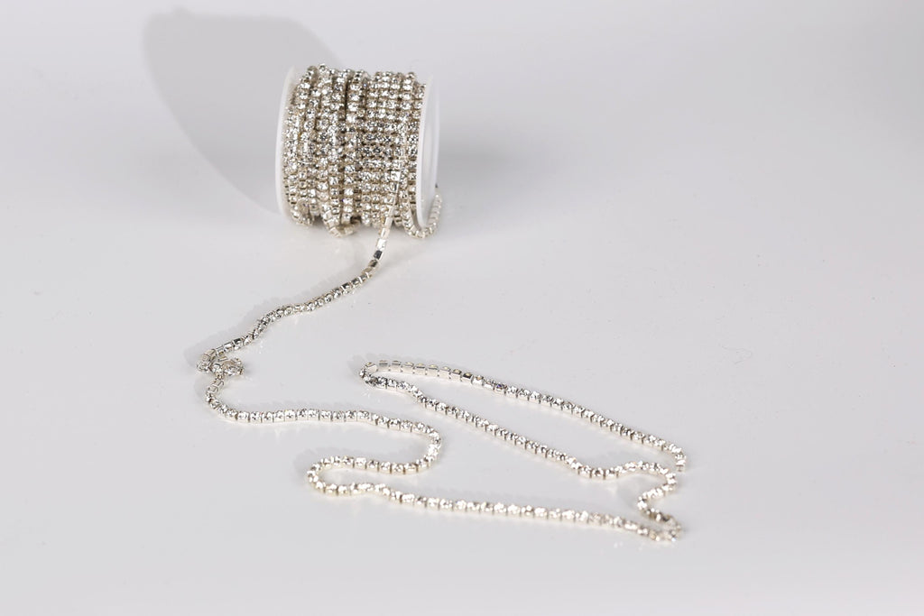 A spool of silver-colored rhinestone wire is lying on a white surface, with the wire extending outwards in a tangled, coiled pattern.