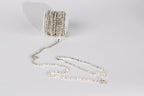 A spool of silver-colored rhinestone wire is lying on a white surface, with the wire extending outwards in a tangled, coiled pattern.