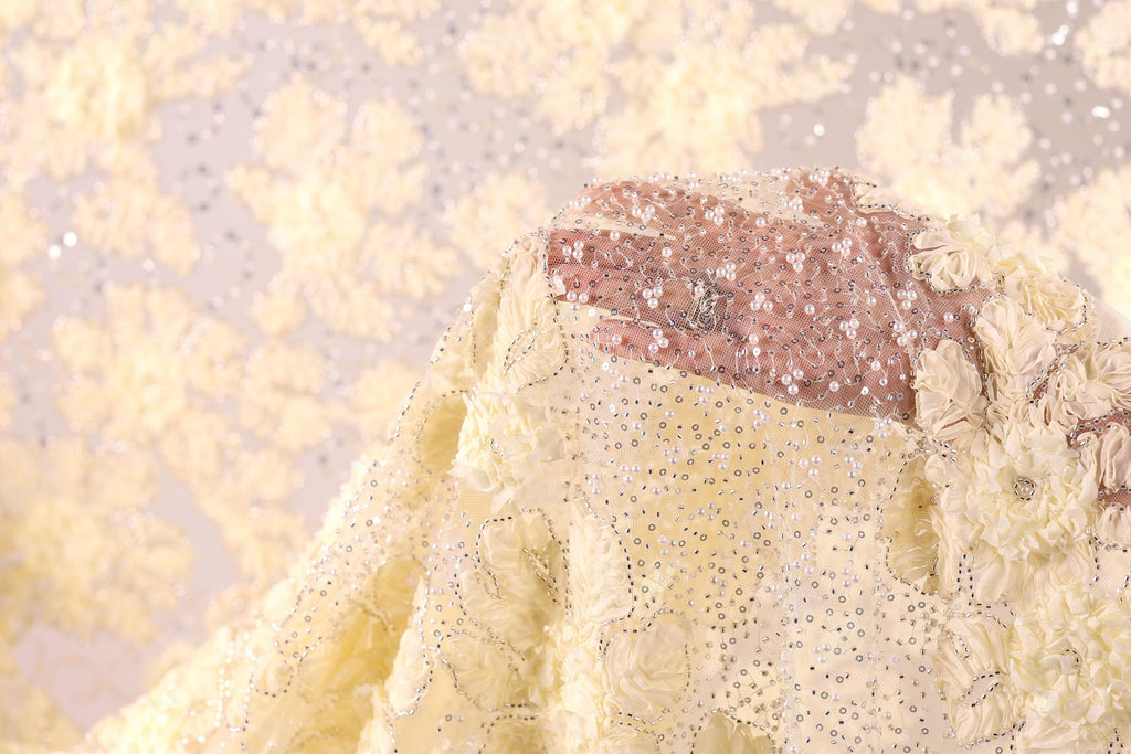 A close-up view of a hand partially obscured by a yellow fabric with a floral pattern, against a background of yellow flowers.