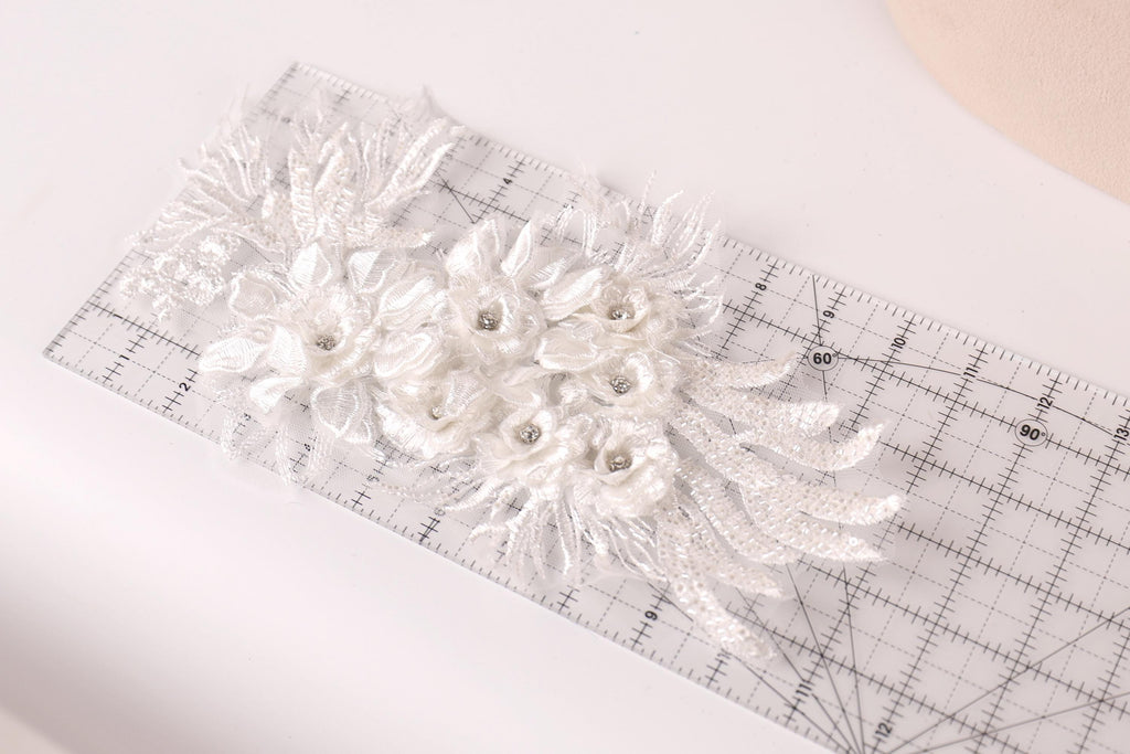 a delicate white lace flower with small silver beads, placed on a transparent ruler.