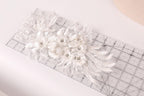 a delicate white lace flower with small silver beads, placed on a transparent ruler.