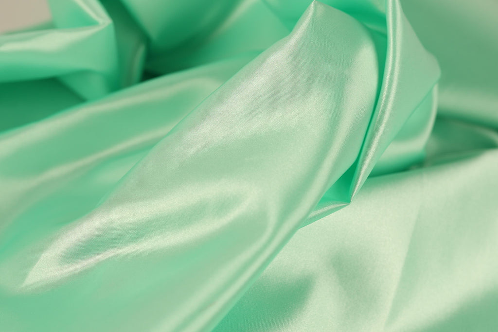 A close-up view of a soft, mint green satin fabric, with its folds and creases creating a textured and flowing appearance.
