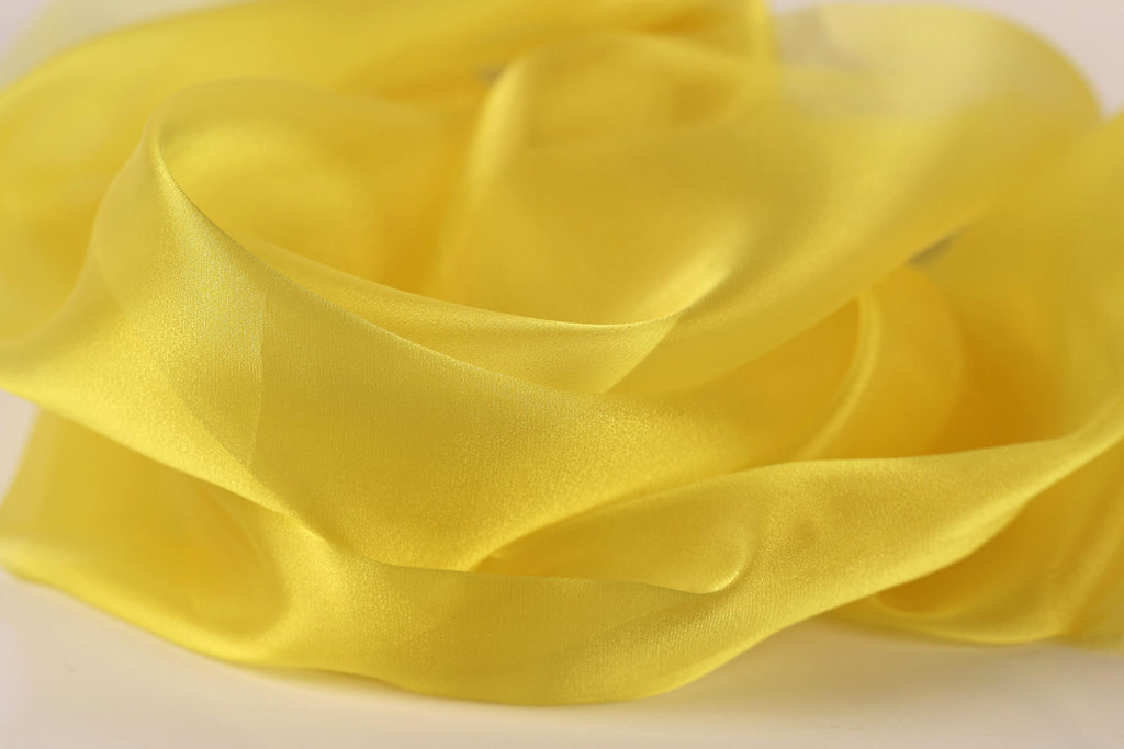 The image is a close-up of a yellow fabric, possibly silk or chiffon, with a soft, flowing texture.