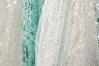 a close-up view of a white fabric with a floral pattern, as well as a fabric with a blue and green floral pattern. The fabrics appear to be made of sequins or other embellishments, adding a touch of sparkle and color to the scene.