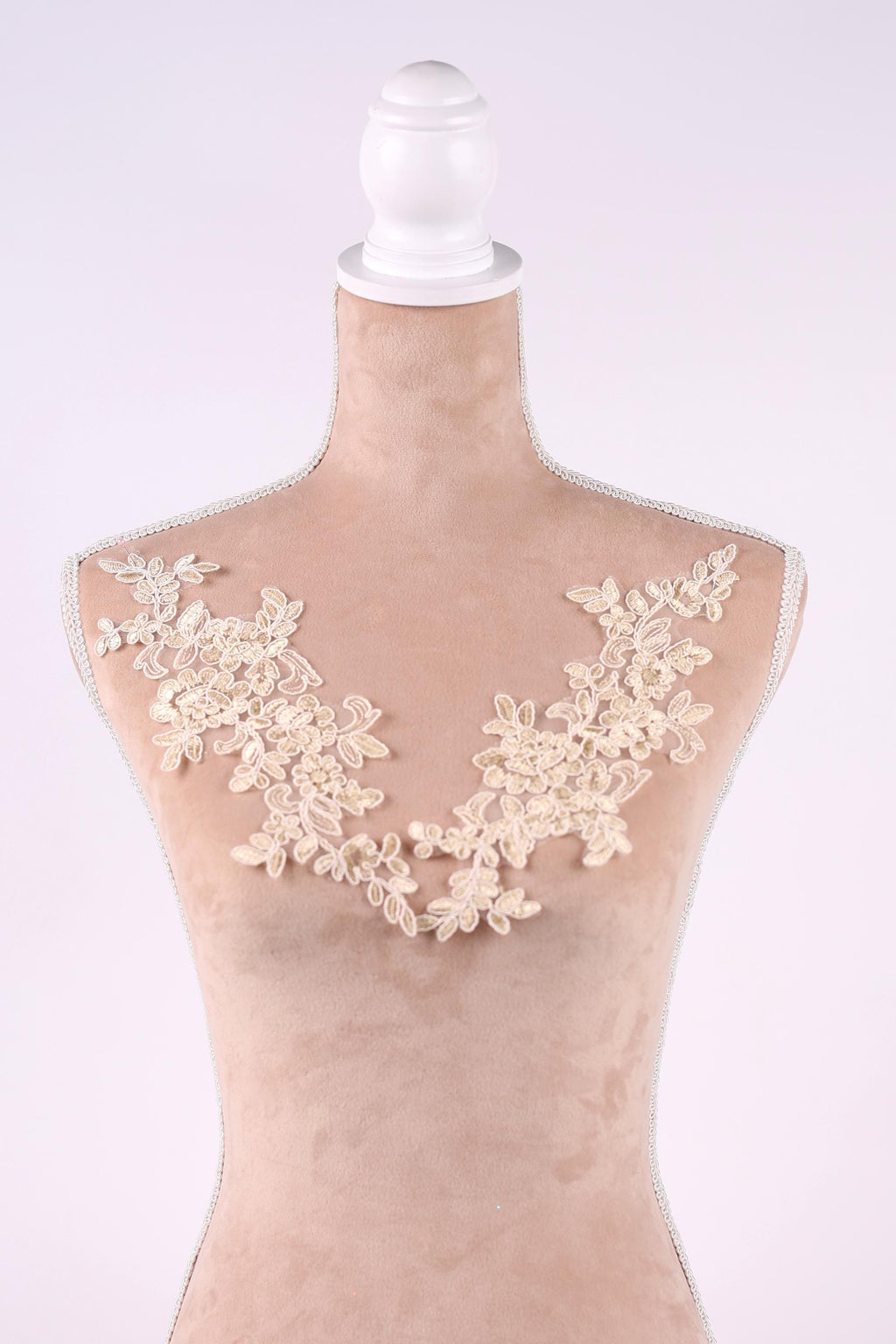A mannequin with a beige body and a white headpiece, adorned with delicate white lace flowers on the bust area.