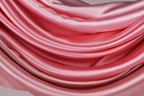 The image is a close-up of a soft, flowing pink satin fabric, with its folds and creases creating a sense of depth and texture.
