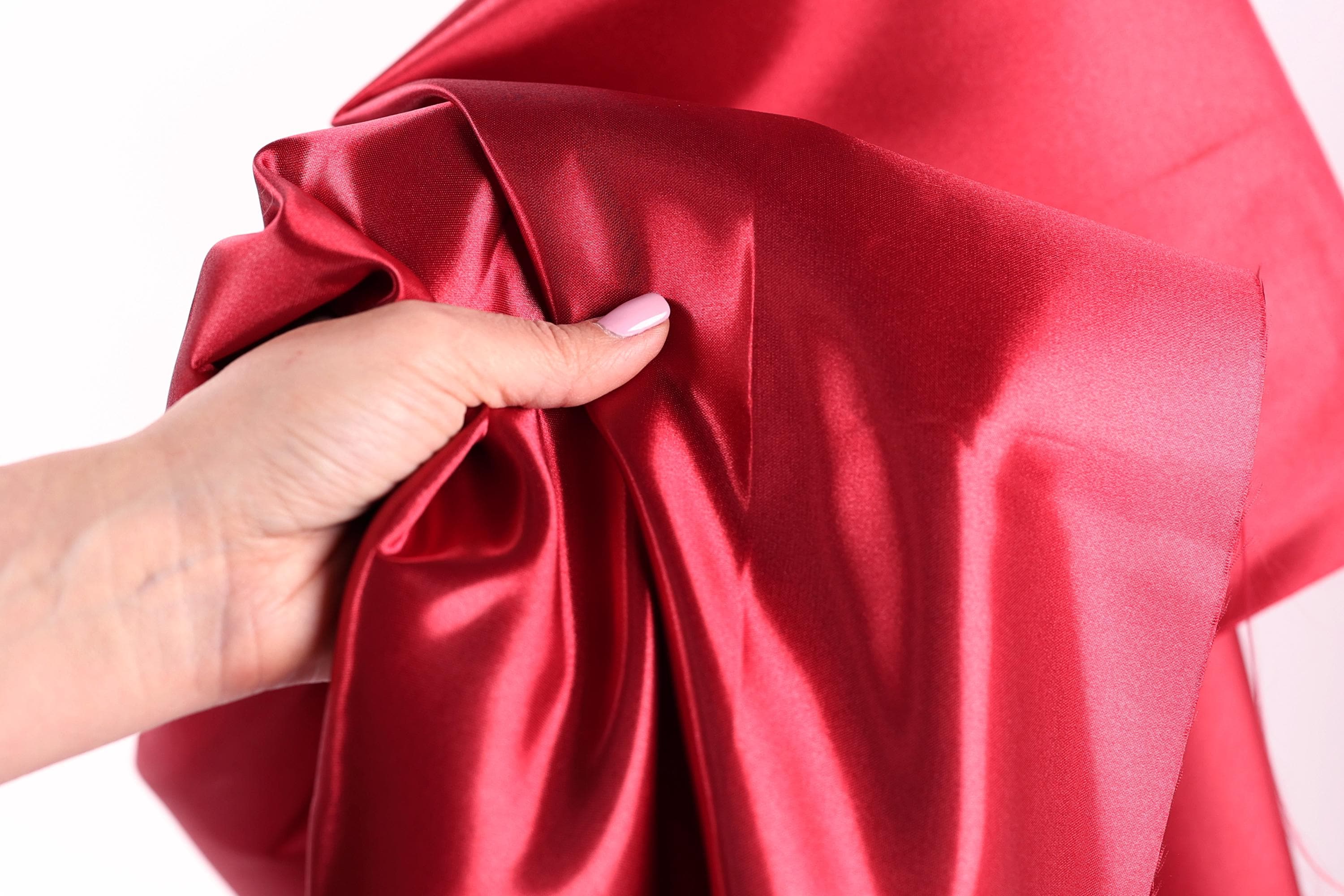 A hand is holding a piece of red satin fabric, with the fabric partially draped over the hand.