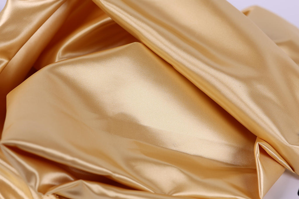 The image is a close-up of a shiny, golden-colored fabric, possibly silk or satin, with a smooth and shiny texture.
