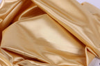 The image is a close-up of a shiny, golden-colored fabric, possibly silk or satin, with a smooth and shiny texture.
