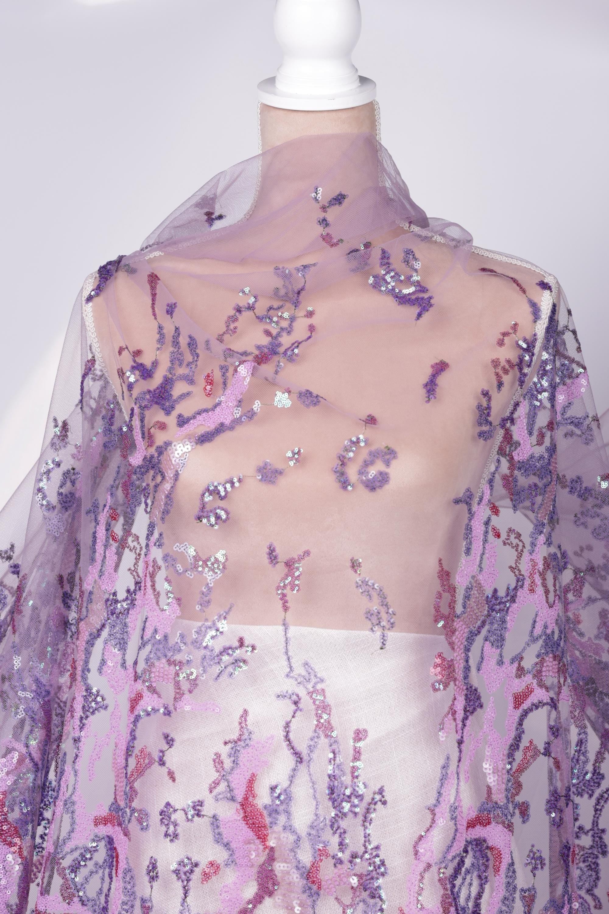 a mannequin wearing a sheer, purple, and pink sequined fabric draped over it.