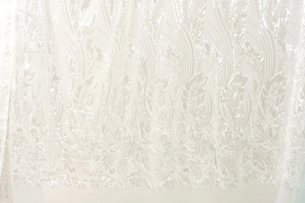 The image is a close-up of a white fabric with a repeating pattern of white leaves or flowers. The fabric appears to be made of a sheer or sheer-like material, which gives it a delicate and airy appearance. The pattern is intricate and detailed, with the leaves or flowers appearing to be made of sequins or glitter, adding a touch of sparkle to the fabric. The image does not contain any text or other discernible objects, and the focus is solely on the fabric and its pattern.