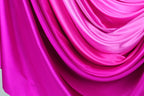 a close-up view of a vibrant, flowing fabric with a gradient of pink and purple colors. The fabric appears to be made of silk or satin, and it is draped in a way that creates a sense of movement and elegance. The colors are rich and intense, with the pink and purple hues dominating the fabric, while the fabric itself has a smooth and shiny texture.