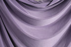 a close-up view of a soft, flowing purple fabric, possibly a curtain or garment. The fabric has a smooth, shiny texture and is draped in a way that creates a sense of movement and depth.