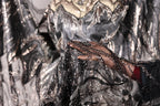A close-up view of a hand holding a piece of black and silver sequined fabric, with a blurred background that appears to be a dress or garment.