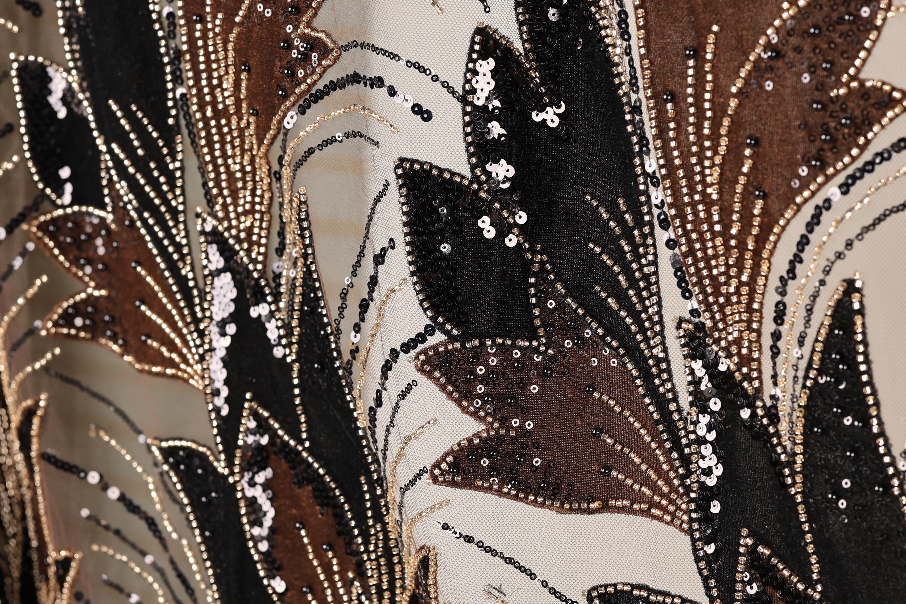 The image is a close-up of a fabric with a floral pattern, featuring a mix of black, brown, and gold colors. The fabric appears to be made of a shiny material, possibly sequin or glitter, and has a textured appearance.