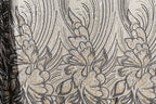 a close-up view of a fabric with a floral pattern. The fabric appears to be made of sequin material, with a repeating pattern of black and gold flowers and leaves. The pattern is intricate and detailed, showcasing the craftsmanship and artistry involved in creating the fabric.